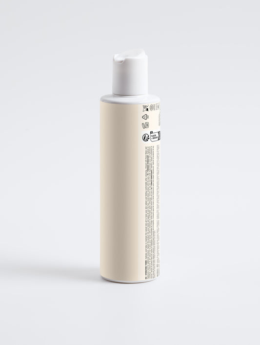 A cream-labelled toner bottle with a white disc-top cap stands on pale grey. Its rear label lists hydrating rose water ingredients in English, French, Spanish.