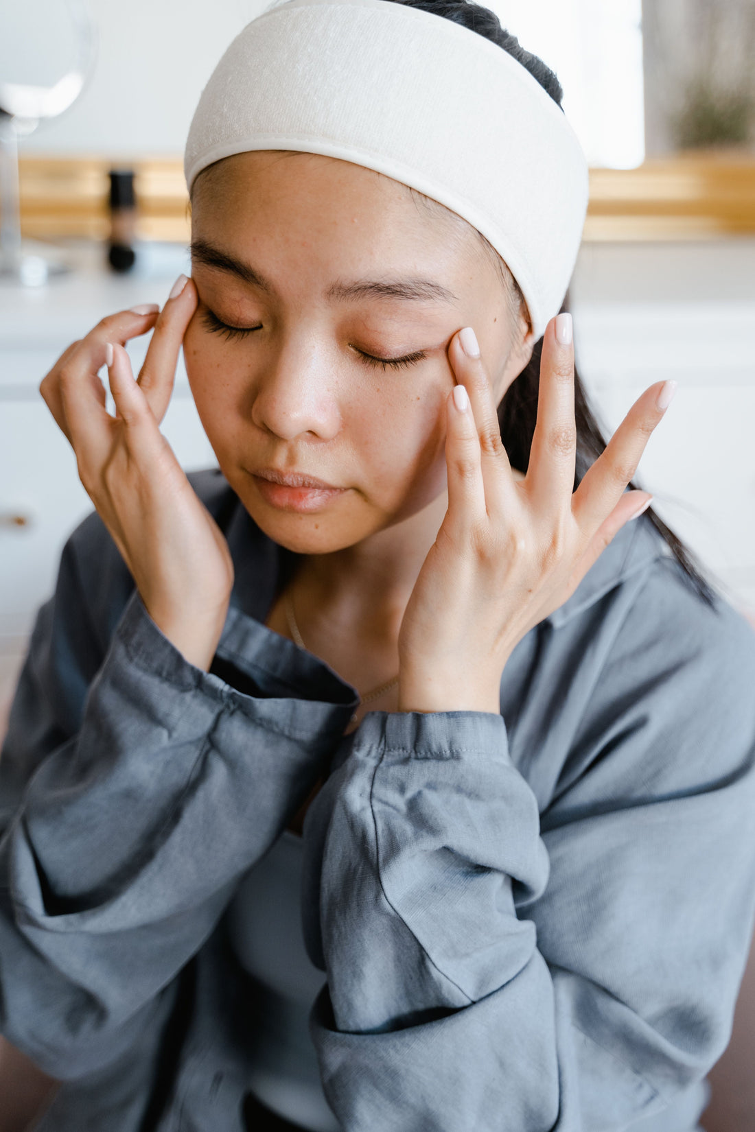 A young South Asian woman is using both hands to simultaneously apply eye cream under her eyes  