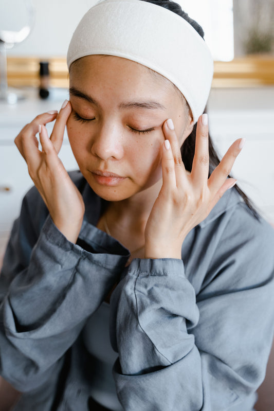 A young South Asian woman is using both hands to simultaneously apply eye cream under her eyes  