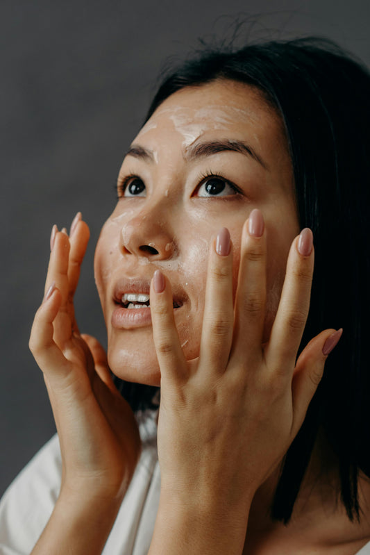 Head-and-shoulders portrait of a young Asian woman applying a skincare product to her face 