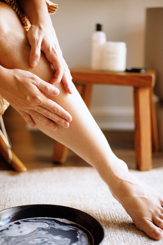 A woman applying body lotion to her left leg