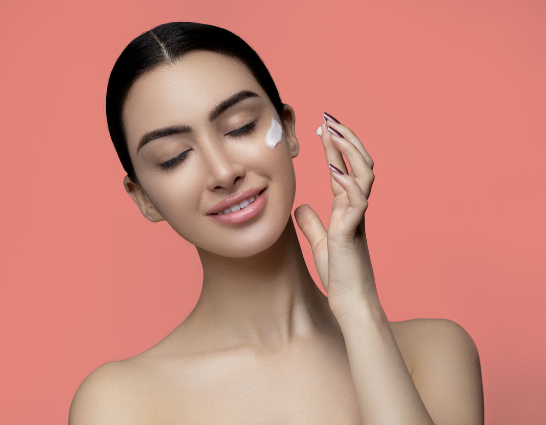 Woman with eyes closed applying skincare cream to her face.