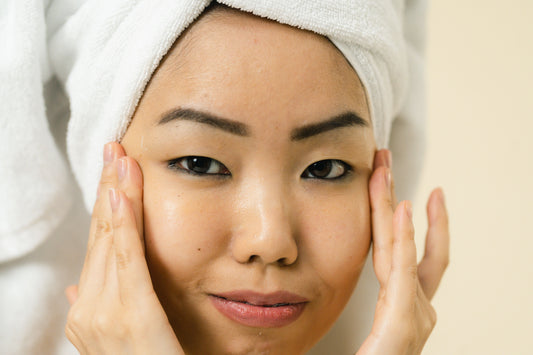 A young Asian woman with glowing skin is shown with her fingertips placed to the sides of her eyes