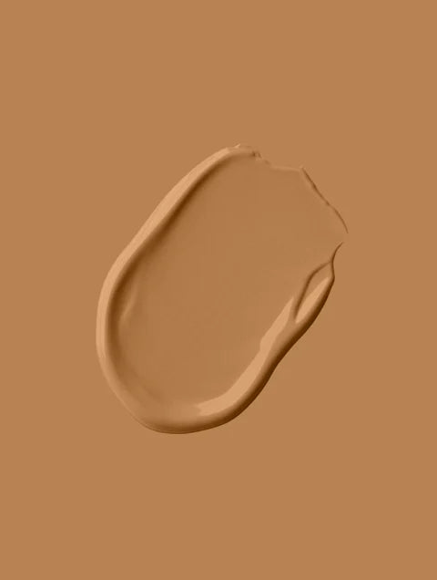 A smooth, creamy swatch of warm beige liquid foundation smeared across a matching tan background, showing its silky texture, soft sheen, and seamless, natural-looking finish.